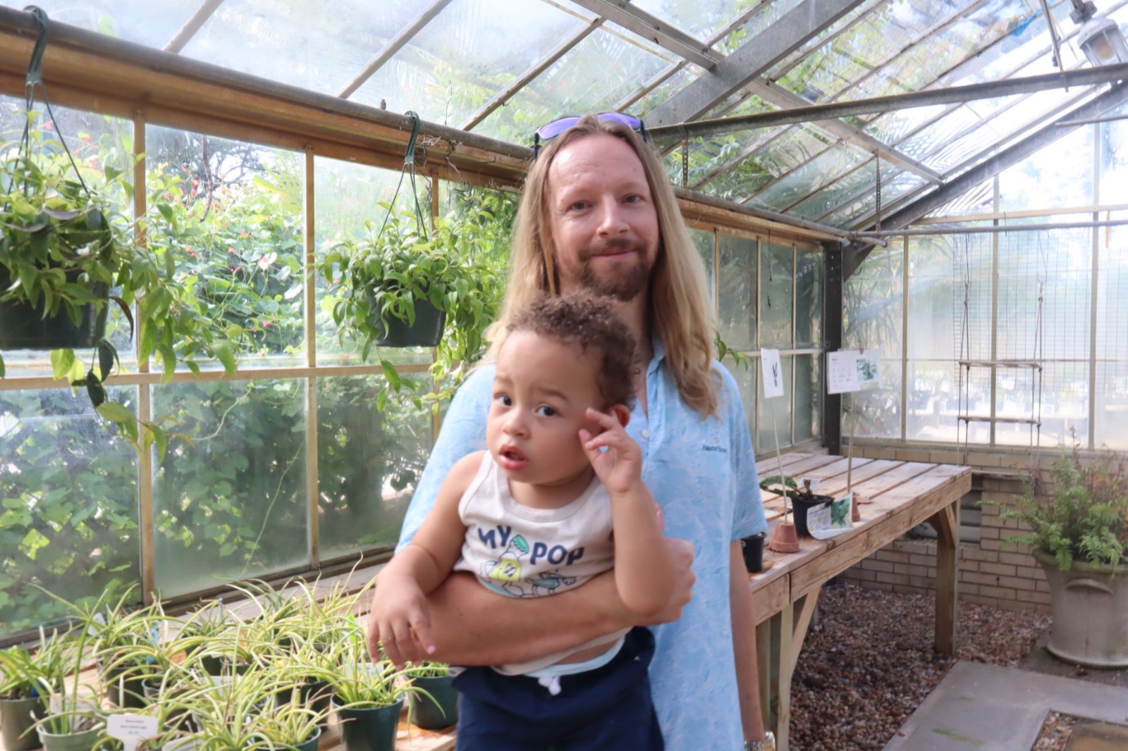 Tampa family photographer captures a father holding his toddler in a sunlit greenhouse